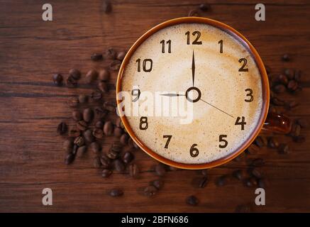 Tazza di caffè in ceramica marrone decorata con fagioli tostati su sfondo di legno. Concetto di tempo Foto Stock