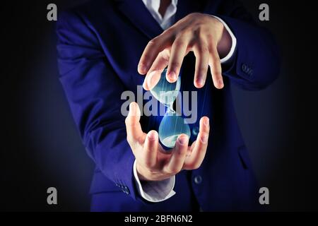 Uomo d'affari che tiene la clessidra in mano su sfondo scuro Foto Stock