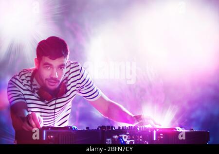 DJ riproduzione di musica al mixer su colorato sfondo sfocato Foto Stock