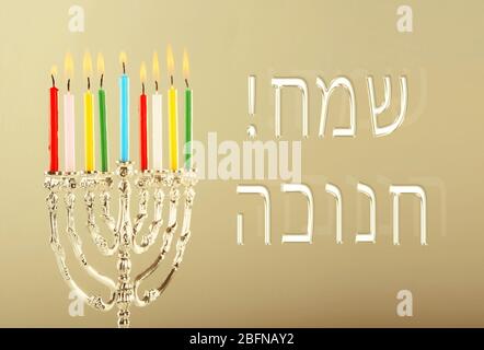 Menorah con candele per Hanukkah su sfondo colorato. Concetto di celebrazione di Hanukkah. Testo HAPPY HANUKKAH in ebraico Foto Stock
