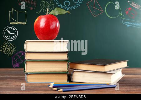 Libri scolastici con mela a tavola. Schizzi creativi sullo sfondo della lavagna. Concetto di sviluppo dei bambini. Foto Stock