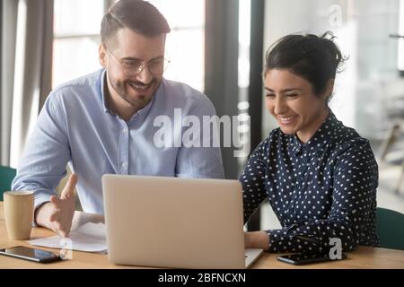 Colleghi multietnici seduti alla scrivania che scherzano sul posto di lavoro Foto Stock
