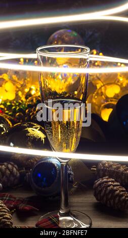 Un bicchiere di champagne sulle decorazioni natalizie. Felice anno nuovo. Composizione di Natale. 2020. Giochi di Natale e luci Garlands. Ristorante, bar pa Foto Stock