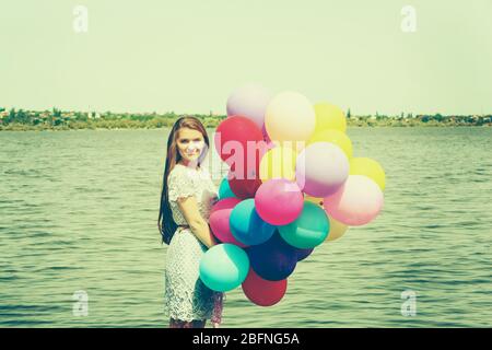 Giovane donna con palloncini colorati sulla riva del fiume Foto Stock