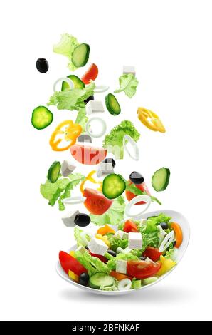 Verdure a fette che cadono in ciotola con insalata su sfondo bianco Foto Stock