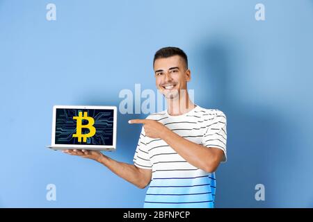 Uomo che tiene un laptop con il simbolo della moneta a forma di bit sullo schermo contro lo sfondo colorato Foto Stock