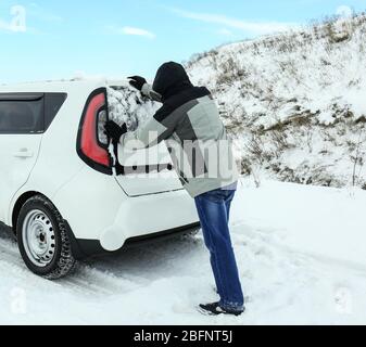 Uomo che spinge la macchina bloccato in moto di neve su strada invernale Foto Stock