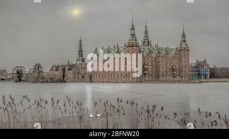 Ghiaccio sul lago al castello di Frederiksborg e due cigni che nuotano in un buco nel ghiaccio in una fredda giornata di nebbia, Hillerod, Danimarca, 6 febbraio 2018 Foto Stock