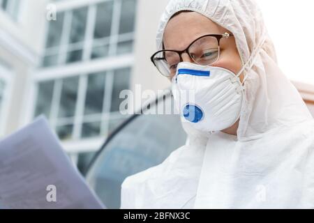 Ritratto di stanco esaurito medico femminile, scienziato o infermiere che indossa maschera facciale e nocciolo biologico ppe tuta lettura Who protocollo di trattamento o. Foto Stock