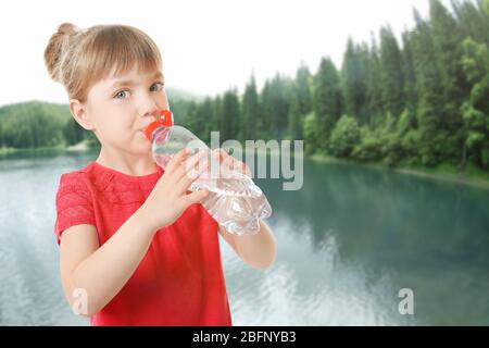 Bambina con bottiglia di acqua pulita su sfondo paesaggistico Foto Stock