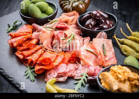 Piatto di antipasti con un misto di salame, prosciutto, chorizo, peperoni, pomodori e olive Foto Stock