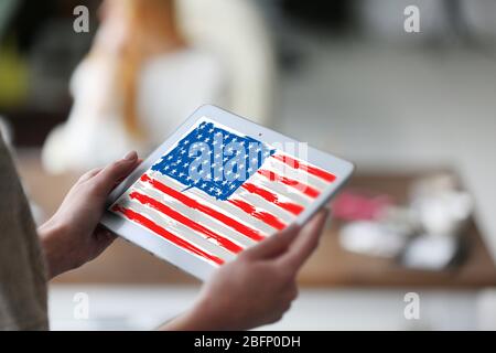 Giovane donna che tiene un tablet con bandiera americana sullo schermo in interni Foto Stock