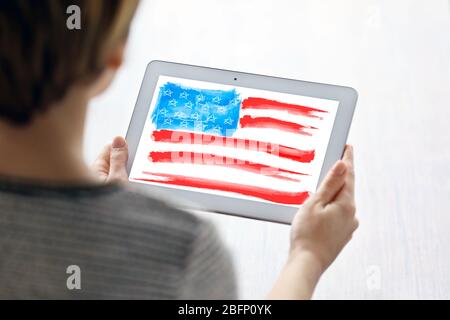 Giovane donna che tiene un tablet con bandiera americana sullo schermo in interni Foto Stock