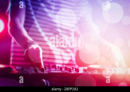 DJ riproduzione di musica al mixer su colorato sfondo sfocato Foto Stock