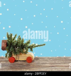 Giocattolo auto in legno che trasporta albero in miniatura di Natale su sfondo colorato Foto Stock