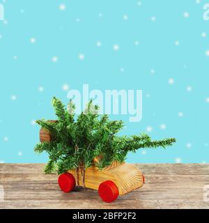 Giocattolo auto in legno che trasporta albero in miniatura di Natale su sfondo colorato Foto Stock