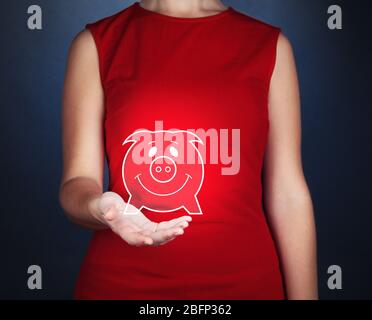 Mano femminile che tiene Virtual Piggy bank su sfondo grigio Foto Stock