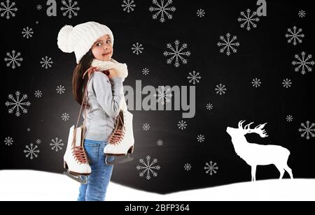 Bambina con pattini in abiti a maglia alla moda e fiocchi di neve disegnati su sfondo lavagna Foto Stock