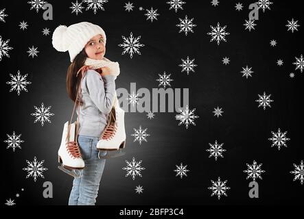 Bambina con pattini in abiti a maglia alla moda e fiocchi di neve disegnati su sfondo lavagna Foto Stock