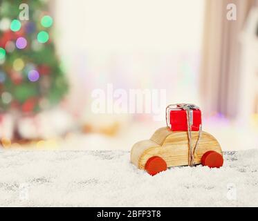 Giocattolo auto in legno che porta Natale in miniatura dono su luci scintillanti sfondo Foto Stock