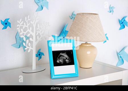 Lampada e cornice fotografica con scansione ecografica del bambino su scaffale nella stanza dei bambini Foto Stock