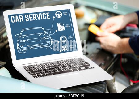 Laptop vicino al motore dell'auto. Programma diagnostico moderno dell'auto sullo schermo. Concetto di assistenza auto. Foto Stock