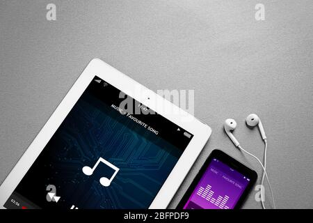 Tablet, smartphone e auricolari su sfondo grigio. Interfaccia lettore musicale sullo schermo. Foto Stock