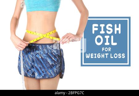 Concetto di olio di pesce per perdita di peso. Donna giovane sottile che misura la vita con nastro e capsule su sfondo bianco Foto Stock