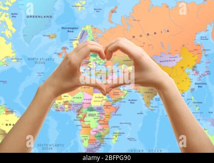 Donna che tiene le mani in forma di cuore e mappa del mondo sullo sfondo. Concetto di terra Foto Stock