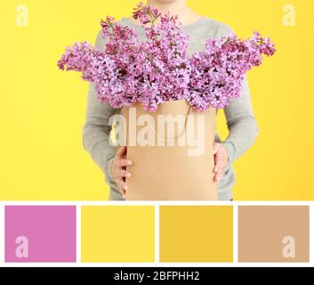 Tavolozza di corrispondenza dei colori. Donna che tiene fiori lilla in sacchetto di carta su sfondo giallo Foto Stock