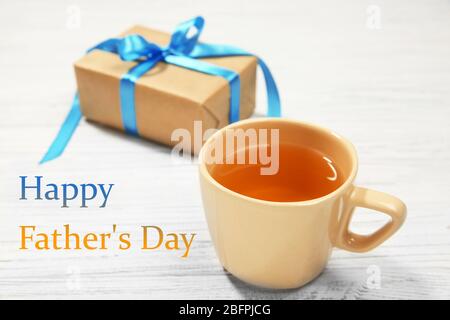 Tazza di tè, scatola regalo e testo HAPPY FATHER'S DAY su sfondo bianco di legno Foto Stock