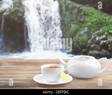 Tazza di tè con pentola e cascata sullo sfondo Foto Stock