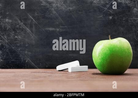 Mela e pezzi di gesso su tavolo di legno contro lavagna della scuola Foto Stock