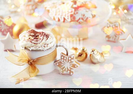 Tazza di cappuccino con gustoso biscotto di pan di zenzero sul tavolo. Belle luci di Natale Foto Stock