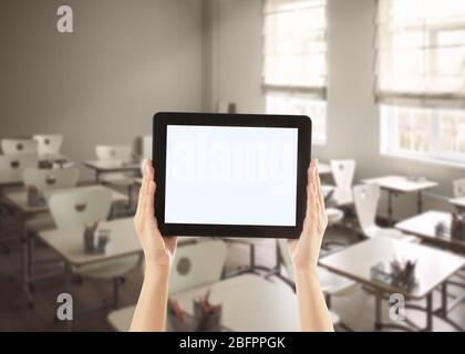 Insegnante che tiene un tablet con schermo vuoto e in aula sullo sfondo. Concetto di scuola e tecnologia moderna Foto Stock