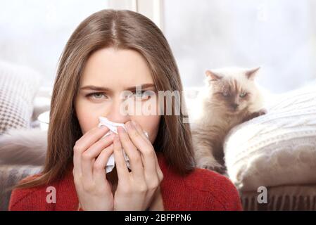 Giovane donna con tessuto e animale domestico sullo sfondo. Concetto di allergie ai gatti Foto Stock