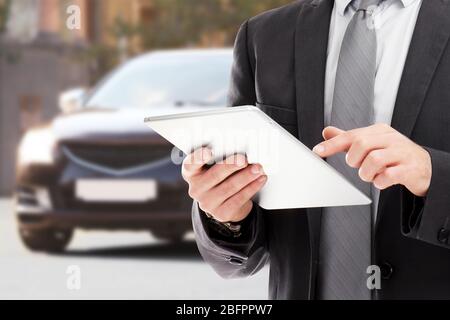 Agente assicurativo che utilizza tablet e auto in background Foto Stock