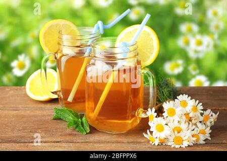 Tè caldo camomilla in vasetti di muratura con fiori su tavolo di legno all'aperto Foto Stock