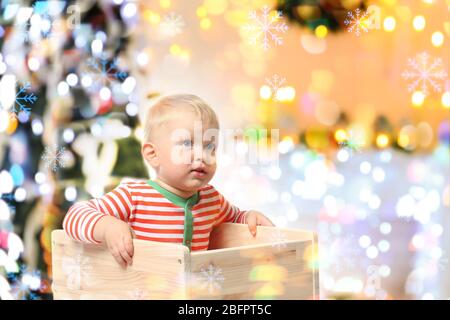 Cute bambino seduto in cassa di legno e albero di Natale sullo sfondo. Concetto di festa di festa Foto Stock