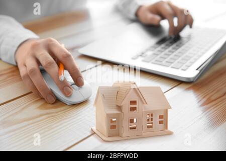 Agente immobiliare che lavora con il laptop e il modello di casa a tavola in ufficio Foto Stock