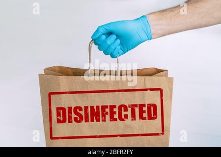 Consegna a casa da negozio online con timbro di sicurezza DISIFINFECTED scritto sul lato cartaceo. Uomo che tiene i generi alimentari con guanto blu medico. Foto Stock