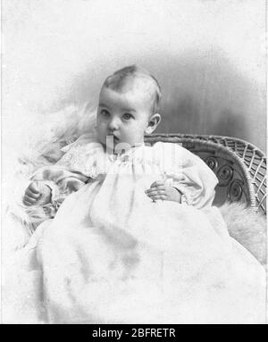 Bambino innocente, con occhi larghi, in bianco, seduto su una sedia di vimini. c.1895. Per vedere le mie altre immagini vintage, Cerca: Prestor vintage Kids Foto Stock