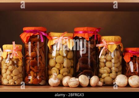 deliziosi funghi marinati nei vasi di vetro e funghi champignons crudi su scaffale di legno Foto Stock