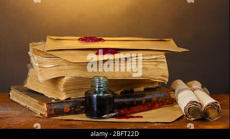 vecchi libri, rotoli, penna a inchiostro e impigliatura su tavolo di legno su sfondo marrone Foto Stock