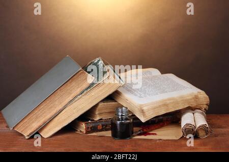 vecchi libri, rotoli, penna a inchiostro e impigliatura su tavolo di legno su sfondo marrone Foto Stock