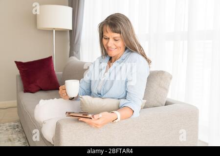 Donna matura che guarda uno schermo tablet nel suo appartamento urbano Foto Stock