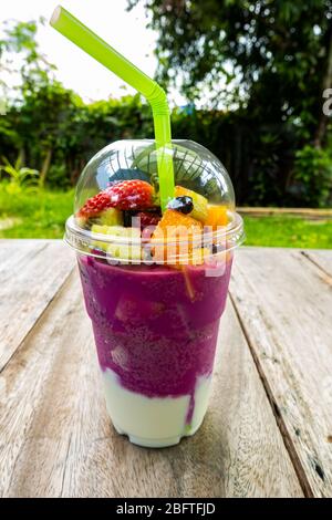 Frutta mista succosa e liscia in una tazza di plastica trasparente su un tavolo di legno. Foto Stock