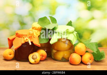 albicocche in scatola in un vaso e albicocche dolci su tavola di legno su sfondo verde Foto Stock