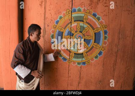 Una guida turistica accanto a una "ruota della vita" a Jakar Dzong, nel quartiere di Bumthang, Bhutan. Foto Stock