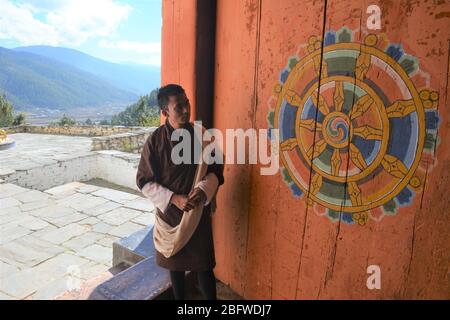 Una guida turistica accanto a una "ruota della vita" a Jakar Dzong, nel quartiere di Bumthang, Bhutan. Foto Stock